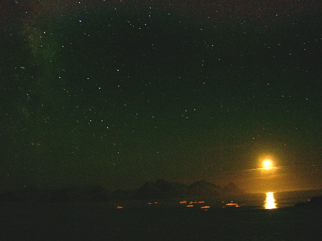 The rising crescent moon illuminating
icebergs, the mountains and casting a path
across the waves.  In the sky to the left are
the star clouds of Sagittarius and Scorpius